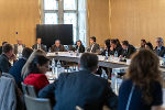 Bildbeschreibung: Gesprächsrunde am Konferenztisch. Diverse Personen sitzen an einem langen Tisch und diskutieren.