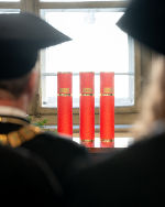 Bildbeschreibung: Szenenbild einer feierlichen Zeremonie, zu sehen sind drei rote Rollen, in denen sich Urkunden befinden.