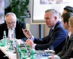 Bildbeschreibung: Konferenzsituation mit Personen in Anzügen, Wasserflaschen und Namensschildern sind zu sehen.