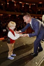 Bildbeschreibung: Ein Mann überreicht einem Kind eine Trophäe. 