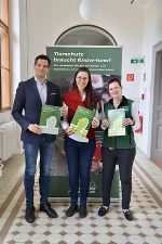 Drei Personen präsentieren Broschüren zum Thema Tierschutz. Im Hintergrund ein Banner mit dem Aufdruck 'Tierschutz braucht Know-how'.