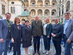 Gruppe von Menschen in formeller Kleidung steht lächelnd vor einem historischen Gebäude mit Arkaden.