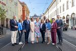 Gruppe von Personen steht lächelnd auf einem belebten Stadtplatz mit historischen Gebäuden im Hintergrund.