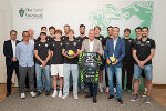 Gruppe von Sportler*innen und Funktionär*innen posieren für ein Foto in einem hellen Raum.