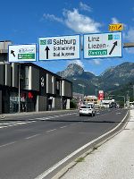 Bildbeschreibung: Straßenansicht mit Beschilderung. Im Hintergrund Berge unter blauem Himmel.