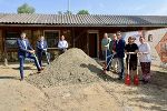 Bildbeschreibung: Gruppe von Menschen mit Schaufeln vor Sandhügel und Holzgebäude.