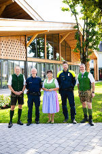 Bildbeschreibung: Gruppe in Tracht oder Uniform vor modernem Gebäude. Sonniges Wetter.