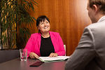 Bildbeschreibung: Gesprächssituation: Eine Person in formeller Kleidung sitzt einem Gesprächspartner gegenüber. Im Hintergrund eine Pflanze und eine Holzverkleidung. #Steiermark #Barrierefreiheit